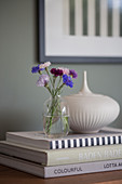 Cornflowers in a glass vase, and a porcelain box on a stack of coffee-table books