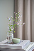 Asters in a glass vase and an earthenware bowl on a stack of coffee-table books