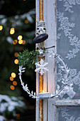 A metal Christmas wreath with a tealight hanging on a window