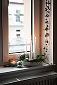 Schale mit Nadelzweigen, Zapfen und Kerzen auf Fensterbank