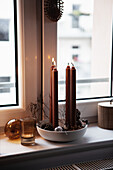 Schale mit Zapfen und Kerzen auf Fensterbank