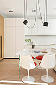 White dining table and white chairs with red seat cushions below pendant light with white fitted kitchen in background