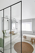 Glass partition in elegant bathroom with washstand, twin sinks, mirrors and marble floor