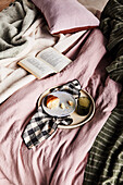Frühstückstablett und Buch auf Bettwäsche