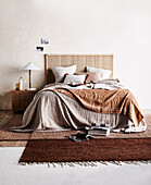 Doppelbett mit Doppelbett mit Kissen und brauner Tagesdecke, farblich passender Teppich und Nachtschränkchen