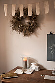 Windlicht auf Holztisch, darüber DIY-Wimpelkette und Kranz an der Wand