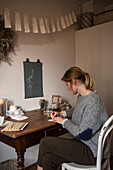 Frau sitzt am alten Holztisch und malt, darüber DIY-Wimpelkette