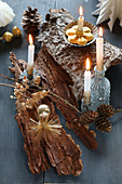 DIY-Adventskranz auf Baumrinde, dekoriert mit brennenden Kerzen auf grauem Holz und goldenem Weihnachtsbaumschmuck