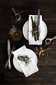 Two place settings with cloth napkins, vintage cutlery and a rosemary sprig on a dark wooden table
