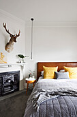 Double bed with leather bed headboard, bedside table, pendant light, fireplace, animal antlers above in bedroom