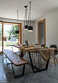 Rustic table with bench and chairs below pendant light in dining room with concrete floor