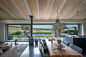 Esstisch aus Holz in offenem Wohnraum mit Glasschiebetür, Blick auf Pool und Landschaft