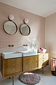 Twin sinks on retro washstand, light pink wall tiles and mirror in bathroom