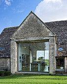 Exterior facade of converted barn with vast window through to kitchen-dining room