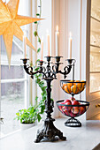 Candlestick with burning candles and fruit baskets on windowsill, illuminated paper star at the window