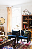 Chairs with blue cushions and antique coffee table in front of bookcase and arched window