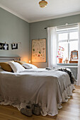 Double bed with long bedspread in bedroom with light grey walls