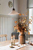 Candles and vintage milk jug with dried branches on a wooden table
