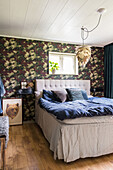 Double bed with an upholstered headboard and wallpaper with floral pattern in the bedroom
