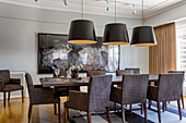 Dining table and grey upholstered chairs below large lampshades