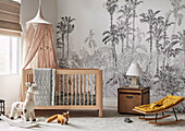 Baby bed with canopy in front of wall with a mural wallpaper