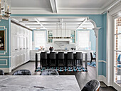 View into the kitchen with white fixtures and light blue walls, kitchen island with bar stools
