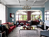 Coffee table, red sofa and armchairs in front of fireplace in living room with white coffered ceiling and light blue walls