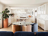 Runder Esstisch mit Marmorplatte und Sessel mit pastellfarbenen Hussen in offener Küche