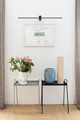 Side tables with vases, above modern art on white wall