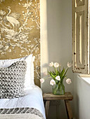 Gold-colored wallpaper as a headboard, stool as a bedside table with a bouquet of tulips