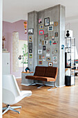 Betonwand als Raumteiler mit Bildern, Fotos und Dekobuchstaben, darunter braune Sessel in offenem Wohnraum