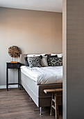 Doppelbett, Nachttisch und rustikale Bank im Schlafzimmer mit hell gestrichener Wand