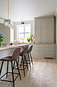 Bar stools at a kitchen island in a country kitchen with grey coffered cabinet fronts