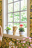 Potted plants on sill of lattice window surrounded by floral wallpaper