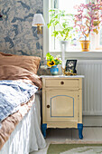 Bedside cabinet next to bed in boy's bedroom with blue and white wallpaper