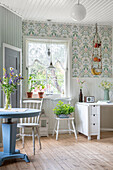 Round table in bright country-house kitchen with window and patterned wallpaper