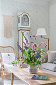Cosy living room with grandfather clock and pale wallpaper: bouquet of summer flowers on coffee table