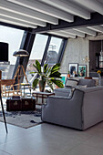 Upholstered furniture, coffee table, houseplant and vintage floor lamp in front of window in a penthouse