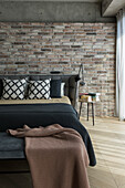 Dressing bench and bed with upholstered headboard against brick wall in bedroom