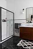 Bathroom with washstand, shower area and black ceramic tiles in marble look