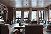 Elegantes Wohnzimmer mit grauen Polstermöbeln, Fenstern, bodenlangen Vorhängen und Holzverkleidung