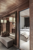 Polsterbank vor Wandspiegel in elegantem, beleuchtetem Flur mit Holzverkleidung, Blick ins Schlafzimmer