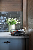 Küchenunterschrank mit Blumen, darüber graue U-Bahn-Fliesen und Holzverkleidung