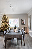 Festively set dining table with grey tablecloth and illuminated Christmas tree in background