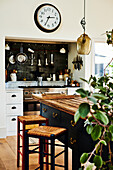 Blaue Kücheninsel mit Arbeitsplatte aus recyceltem Holz, Barhocker und Wanduhr über Gasherd
