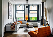 Graues Ecksofa, Couchtisch, Lowboard mit Kaminofen und orangefarbener Zweisitzer im Wohnzimmer