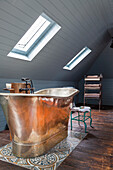 Copper bathtub under sloping roof on rustic floorboards