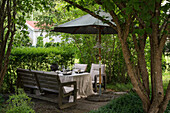 Gedeckter Tisch, Gartenbank, Stühle und Sonnenschirm auf Terrassenplatz