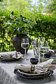 Table set with ceramic plates, linen tablecloths and wine glasses in garden