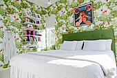 Double bed with green headboard and bookshelf in bedroom with floral wallpaper